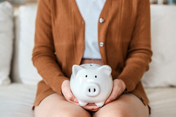 Woman hand holding piggy bank while sitting on sofa. Save money and financial investment