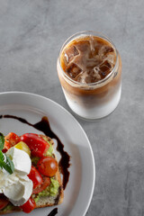 A view of a French vanilla coffee beverage in a can shaped glass, with a plate of avocado toast.