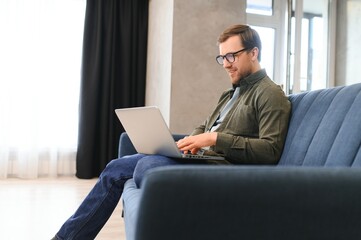 Young cheerful man sitting on sofa with laptop