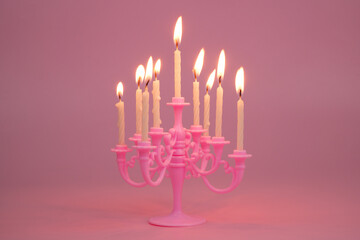 Pink candelabra with many white burning candles on pink background.