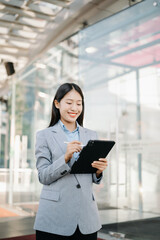 Asian business woman leader entrepreneur, professional manager holding digital tablet computer uon the street in big city on business center background.