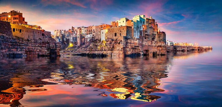 Grotta Palazzese in Polignano a Mare town reflected in the calm waters of Adriatic sea. Exciting summer sunset in Puglia region, Italy, Europe. Travel the world..