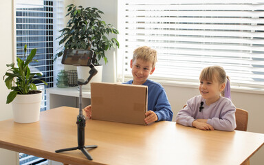 Kids recording an unboxing video for their vlog, smiling and excited as they reveal the contents of...