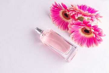Glass bottle of pink perfume on white satin background with flowers gerberas . The concept of natural floral scents. top view. A copy space.