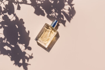 An elegant bottle of cosmetic spray or perfume on a light background among the shade of tree branches. Sunlight. copy space. top view.