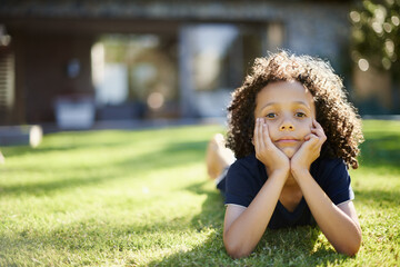 Happy, nature and portrait of child in backyard relaxing on grass for development or fun in...