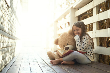 Fototapeta na wymiar Outdoor, book and portrait of girl with teddy bear on floor for storytelling, education and learning. Boardwalk, ground and kid with story in backyard for playful, knowledge and child development