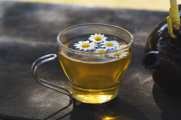 glass cup with a natural camomile tea and a ceramic teapot on a wooden table