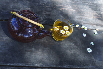 glass cup with a natural camomile tea and a ceramic teapot on a wooden table
