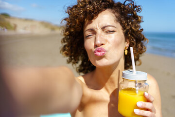Playful woman pouting lips while having juice on beach