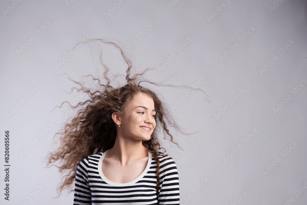 Wall mural Portrait of a gorgeous teenage girl with curly hair, blowing in wind. Studio shot, white background with copy space