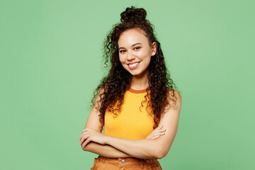 Young smiling cheerful woman of African American ethnicity wear yellow tank shirt top hold hands crossed folded look camera isolated on plain pastel light green background studio. Lifestyle concept.