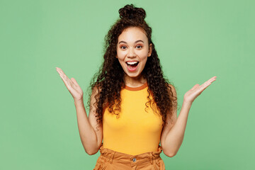 Young surprised fun shocked woman of African American ethnicity wear yellow tank shirt top look camera spread hands say wow isolated on plain pastel light green background studio. Lifestyle concept.