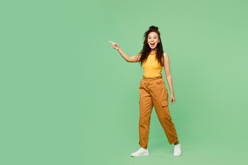 Full body young woman of African American ethnicity wears yellow tank shirt top walk go point index finger aside on area isolated on plain pastel green background studio portrait. Lifestyle concept.