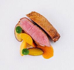 Gourmet duck breast with peach slices on white plate