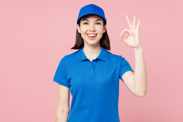 Professional happy delivery girl employee woman wear blue cap t-shirt uniform workwear work as dealer courier showing okay ok gesture isolated on plain pastel pink background studio. Service concept.