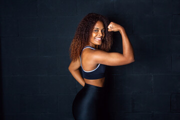 Mujer deportista mostrando biceps. Biceps de mujer. Chica en gimnasio. Fondo negro. Mujer con ropa de deporte. Chica sonriente. Estilo de vida saludable