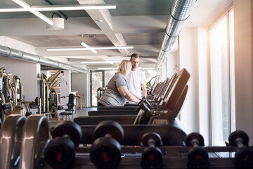 Overweight woman exercising on treadmill in gym. Personal trainer helping her.