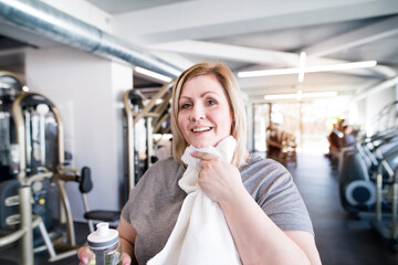 Overweight woman resting after workout in gym. Wipe sweat from face with towel.