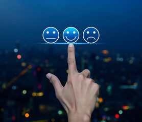 Hand pressing excellent smiley face rating icon over blur colorful night light city tower and...