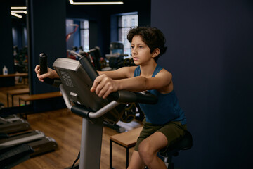 Preteen boy exercising on stationary bike enjoying self training at gym