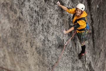 A woman is climbing a rock wall with a yellow jacket and a white helmet