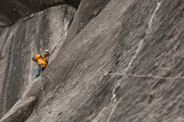 A man in a yellow jacket is climbing a rock wall