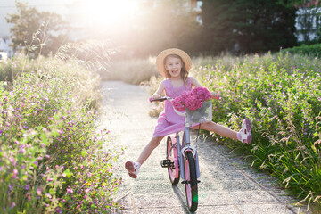 Kid learning to ride bike in park. Child girl in straw hat having fun on bicycle on summer holiday,...