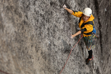 Obraz premium A woman is climbing a rock wall with a yellow jacket and a white helmet