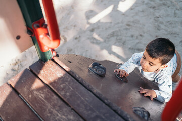 Young autistic boy climbing on playground equipment. Little boy in casual wear is focused on...
