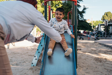 Obraz premium Autistic child playing on slide at park with parent. Excited child sliding down a playground slide with parent's help
