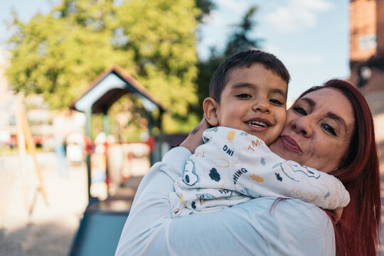 Loving embrace at the playground. Joyous mother hugs her autistic smiling young son at a sunny playground