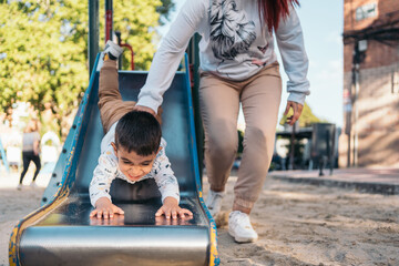 Joyful playtime at the park with mom. Laughing autistic boy slides down as his mother cheers him on...