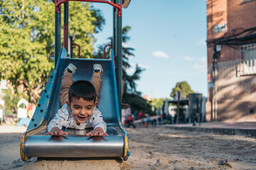 Little autistic boy enjoying slide at playground. Happy child slides down with a big smile in a...