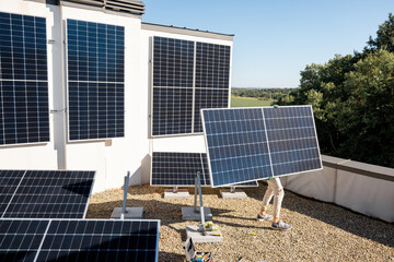 Man carries solar panel while installing solar plant on a rooftop of his property, wide view. Renewable energy for self consumption concept. Idea of installing panels for households