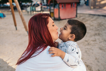 Affectionate embrace between mother and autistic son in playground. Heartwarming moment as a mother...