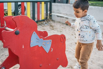 Young autistic boy playing with red rocking horse at playground. Little boy enjoys outdoor playtime...