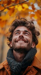 portrait of a smiling man with beard and brown hair wearing an orange jacket and scarf looking up at the sky