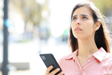 Worried woman holding phone looking up