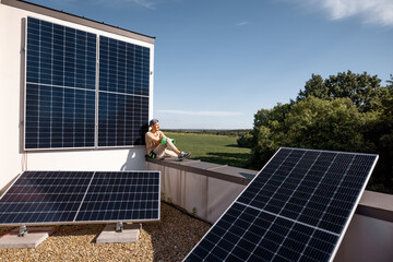 Man sitting on a rooftop of his house with a solar power station installed on it. Renewable green...