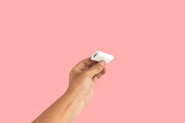 Black male hand holding a USB charger plug isolated on pink background