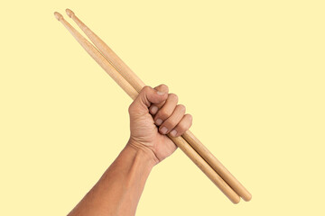 Black male hand holding wooden Drum sticks isolated on yellow background