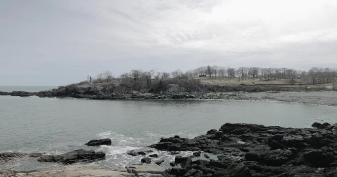 Pan across the beautiful rocky sea side view of the Portland Maine revealing the Head Light light house during a beautiful spring day with waves rolling into the rocky shore in 4k.