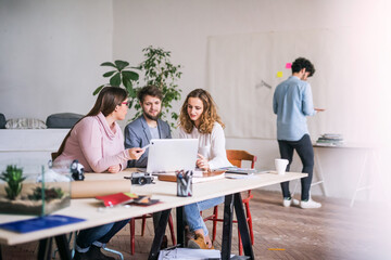 Young group of colleagues working on a new project together in a startup company office. Working in co-working space.