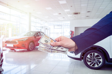business man gives dollar cash when buying a car at showroom. Concept of purchase or rent vechicle