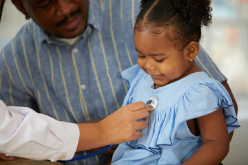 closeup doctor hands holding stethoscope and listening to African child patient's breath beside her...