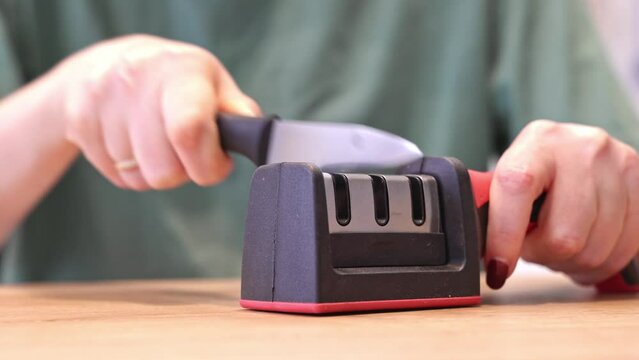 Close-up of woman sharpening knife with special knife sharpener at home	