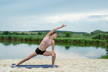 young fitness woman doing streching exercise on lake beach in summer