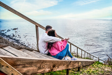 Young married couple sitting on the wooden long stairs and looking at Japanese sea