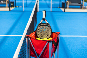 Paddle tennis: Padel racket and ball in front of an outdoor court.